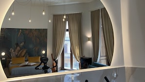 A modern hotel room with a large mirror, a bed with a blue bedspread, a desk with a chair, and a bike in the corner. - La Lepre Felice (Naples)