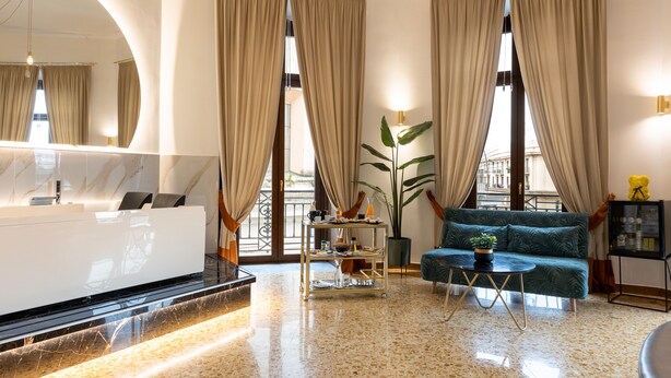 A modern hotel lobby with a reception desk, a green sofa, a coffee table, and large windows with curtains. - La Lepre Felice (Naples)