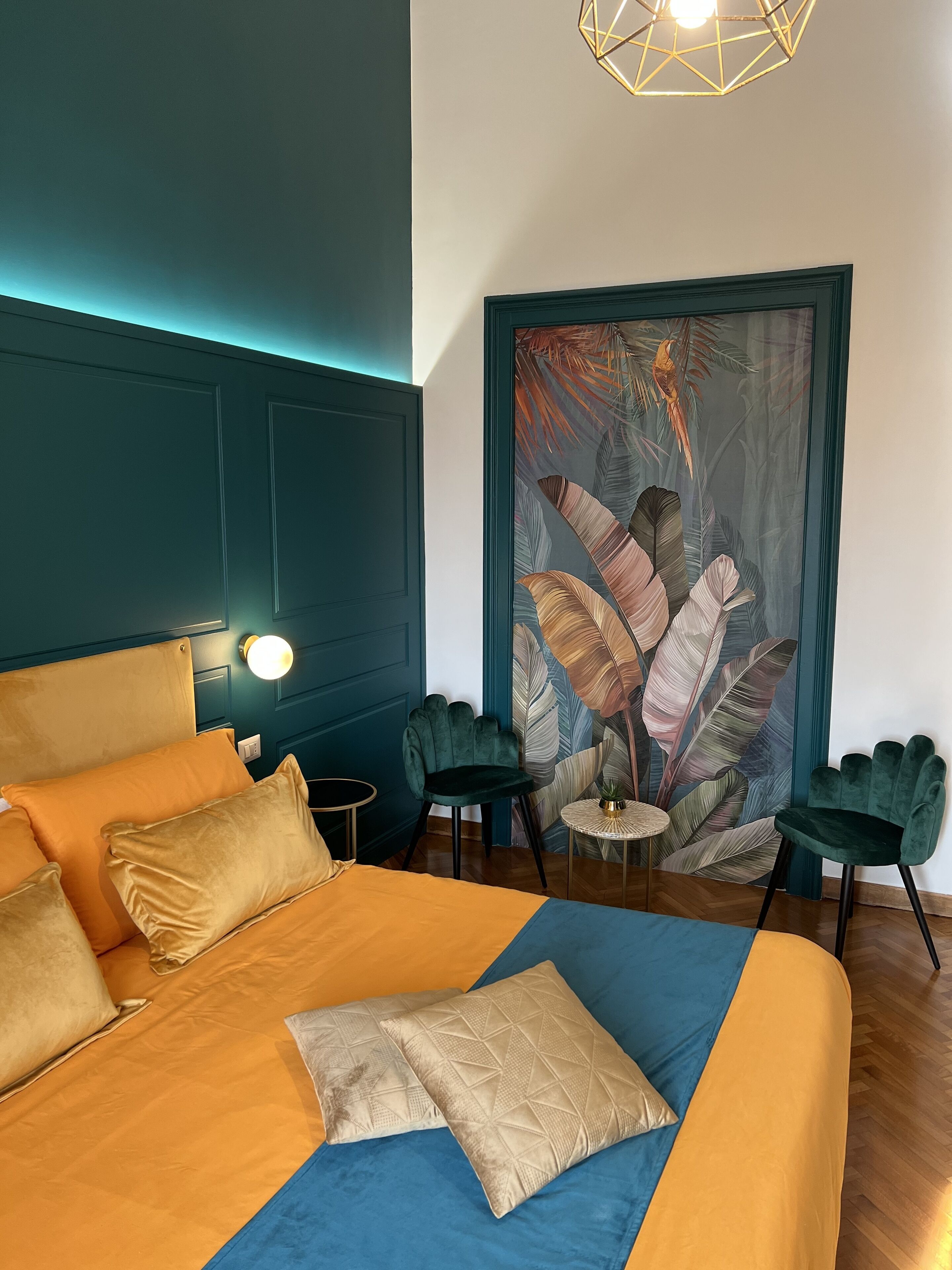 Een slaapkamer met een groot bed, twee stoelen, een klein tafeltje en een wanddecoratie.