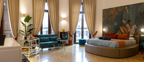 Un salon moderne avec un canapé rond, un fauteuil vert, une petite table et un grand tableau accroché au mur.