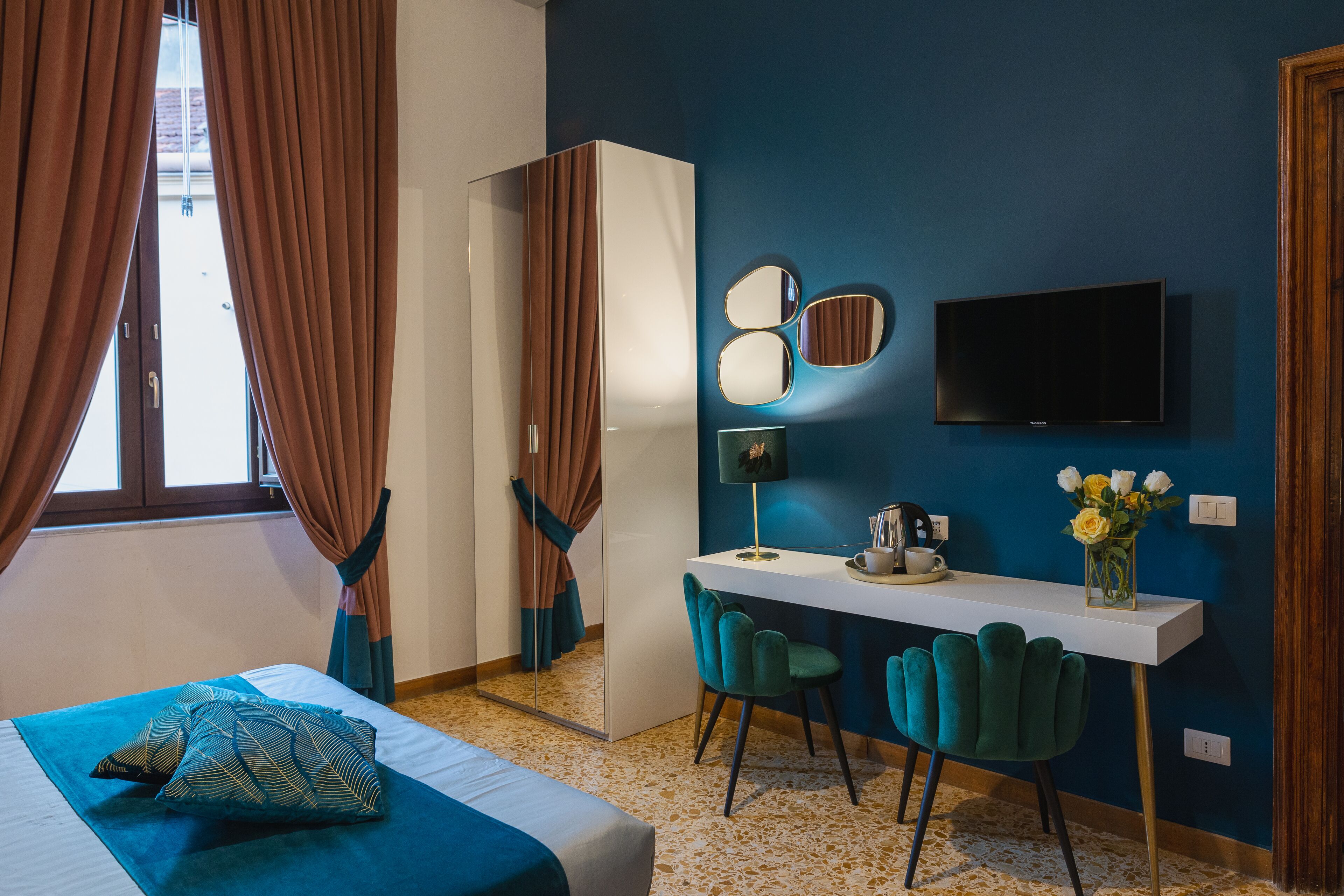 Una camera d'albergo con un letto, una scrivania con due sedie, una televisione e uno specchio a parete.