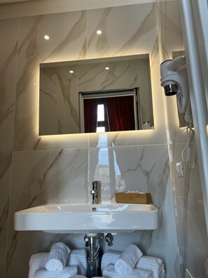 A bathroom with a marble wall, a sink with a mirror above it, and a shower area. - La Lepre Felice (Naples)