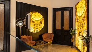 A modern interior with a staircase, two armchairs, a floor lamp, and a wall with a golden architectural design. - La Lepre Felice (Naples)
