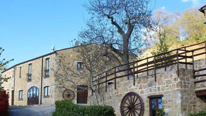A stone building with a gravel driveway, a wooden fence, and a large wooden wheel. - Agriturismo Grotta Dell'Eremita (Castelmezzano)