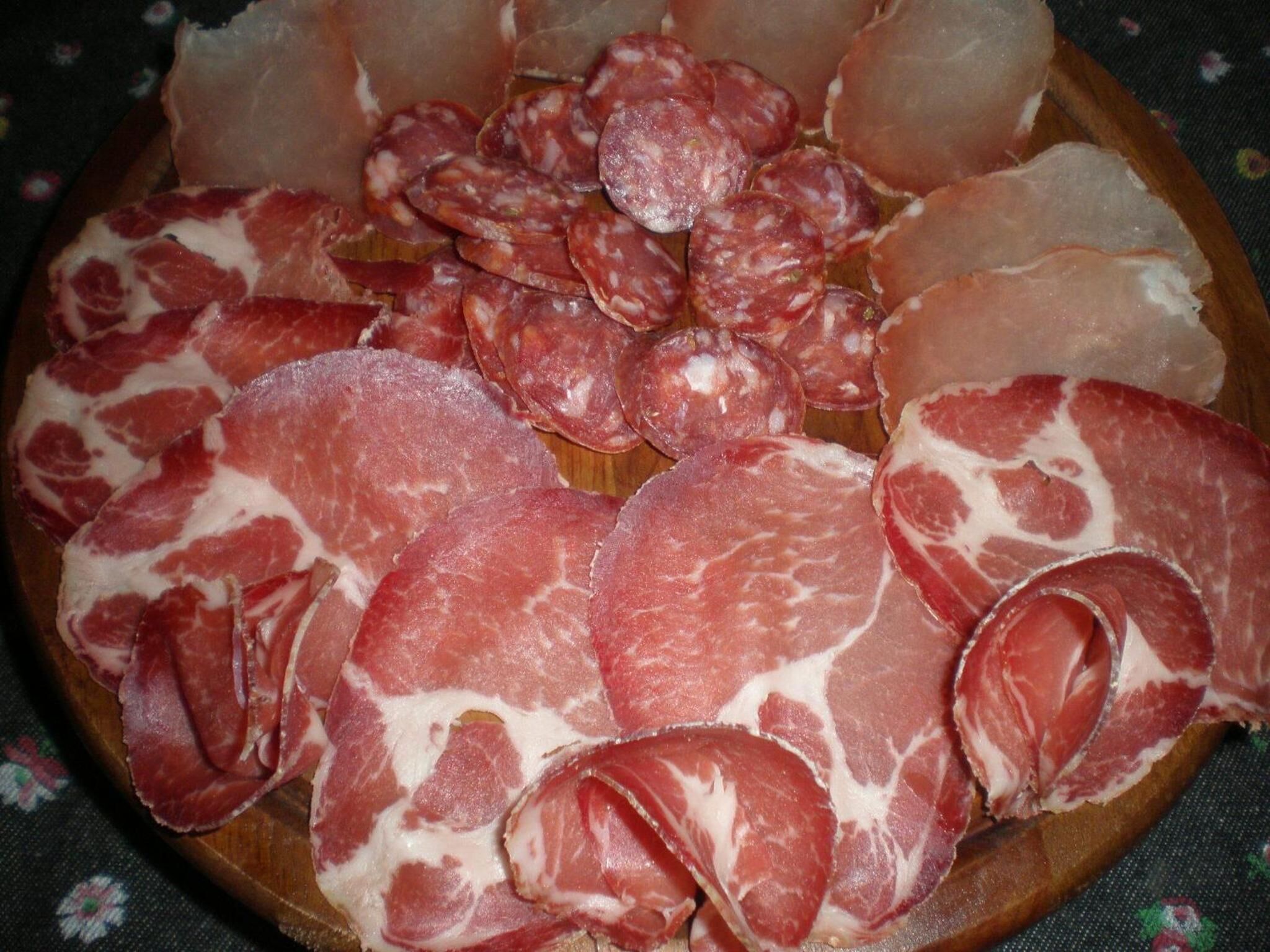 Un tagliere di legno con diversi tipi di salumi, tra cui salame e prosciutto.