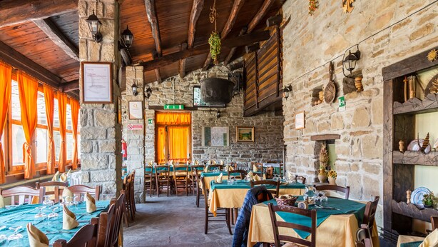 A restaurant with stone walls, wooden beams, and tables set for dining. - Agriturismo Grotta Dell'Eremita (Castelmezzano)