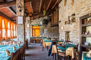 Un restaurante con paredes de piedra, vigas de madera y mesas preparadas para comer.