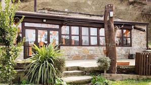 A rustic stone building with a wooden porch and a large window. - Agriturismo Grotta Dell'Eremita (Castelmezzano)