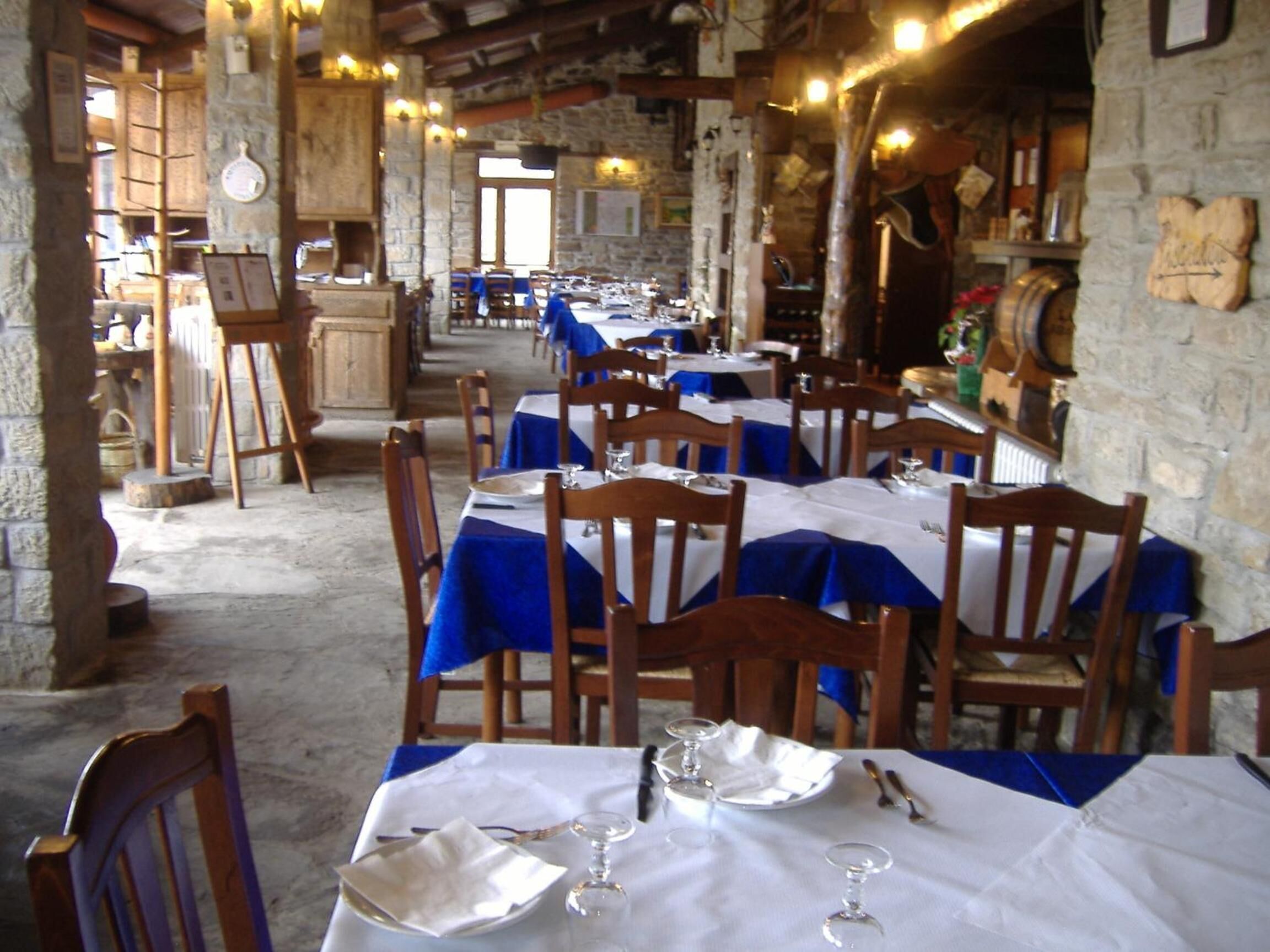 A restaurant with stone walls and wooden furniture, featuring tables set with white tablecloths and blue napkins.