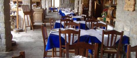 A restaurant with stone walls and wooden furniture, featuring tables set with white tablecloths and blue napkins.