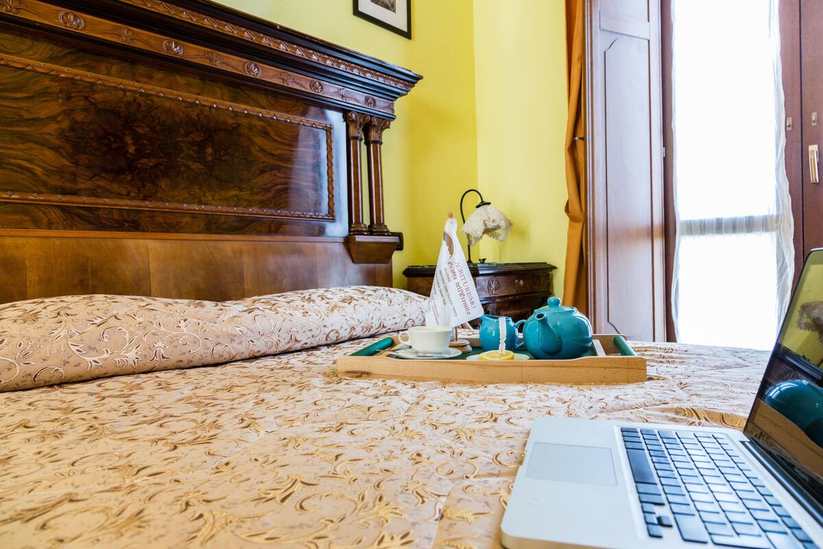 Una cama con un ordenador portátil, una bandeja con tetera y taza, y una lámpara.