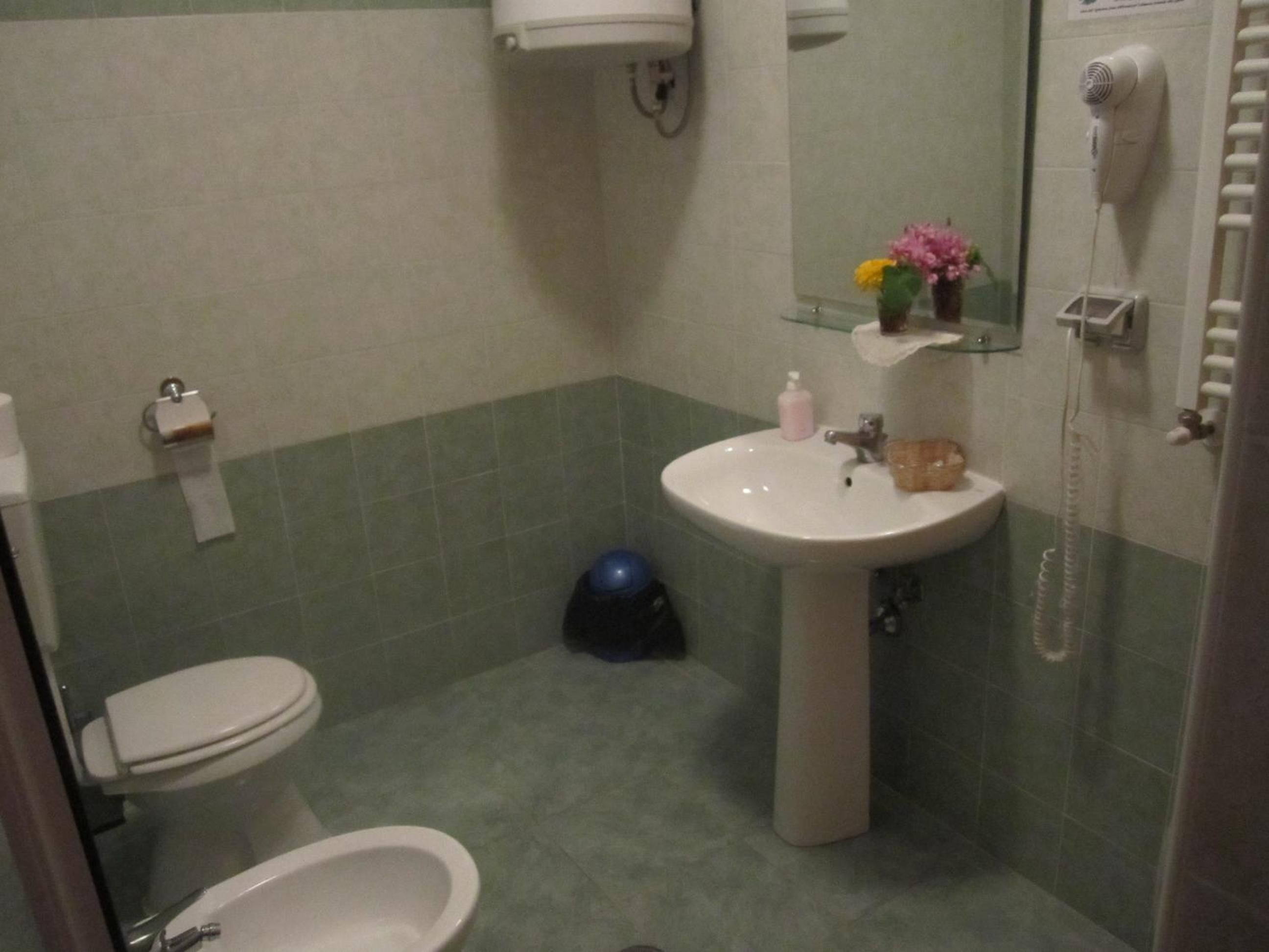 A bathroom with a toilet, bidet, sink, and a hairdryer mounted on the wall.