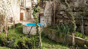 A rustic stone building with a wooden staircase leading to a door, a small pool, and overgrown vegetation. - Agriturismo Grotta Dell'Eremita (Castelmezzano)