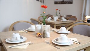 A dining table set with white dishes, a vase with a single red flower, and salt and pepper shakers. - Hotel Pilar Garni (Cologne)