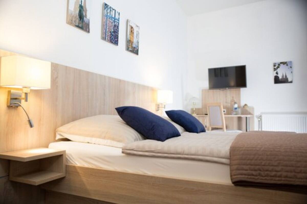 A hotel room with a bed, bedside table, lamp, TV, and artwork on the wall.