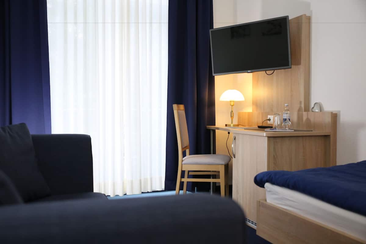 A hotel room with a bed, a desk with a lamp, a TV mounted on the wall, and a chair.
