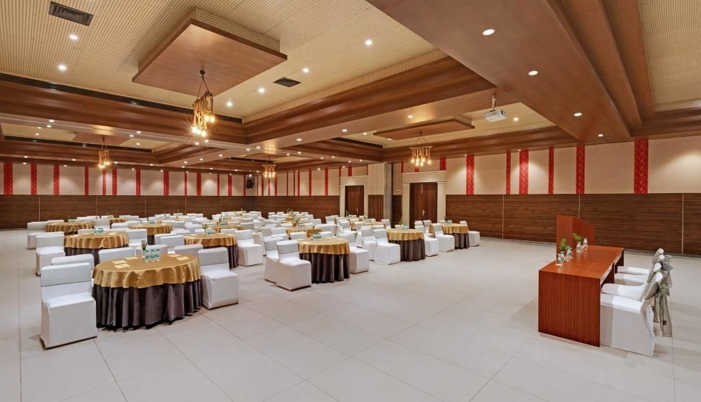 Une grande salle de conférence dotée de plusieurs tables rondes et de chaises blanches, de lambris en bois sur les murs et d’une estrade avec un pupitre.