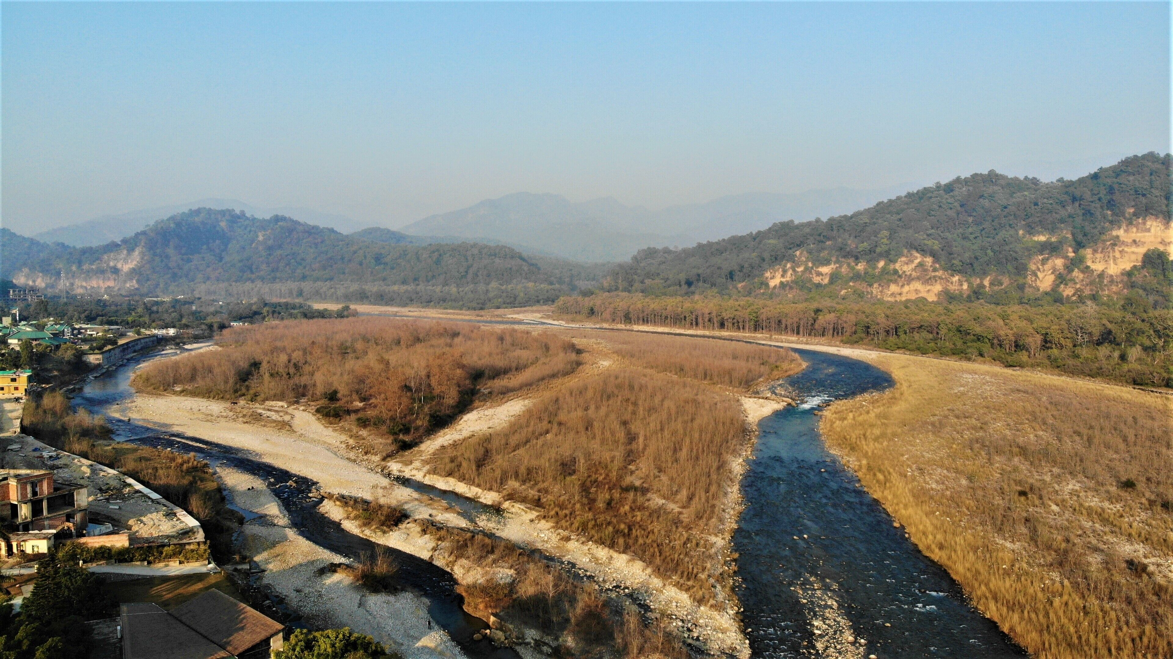 A river meandering through a valley with a town on one side and mountains in the background.