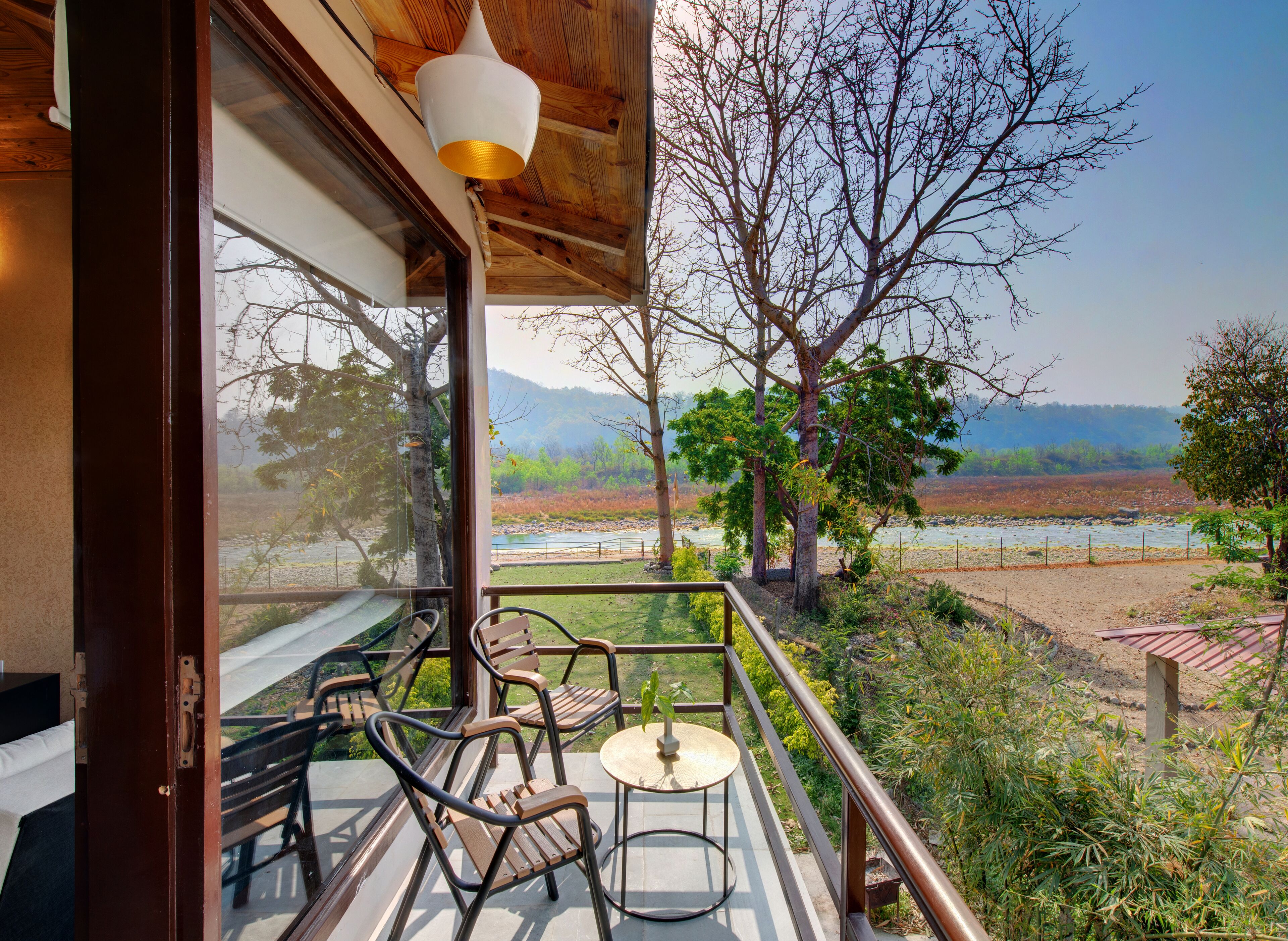 A balcony with wooden chairs and a small table, overlooking a river and trees.