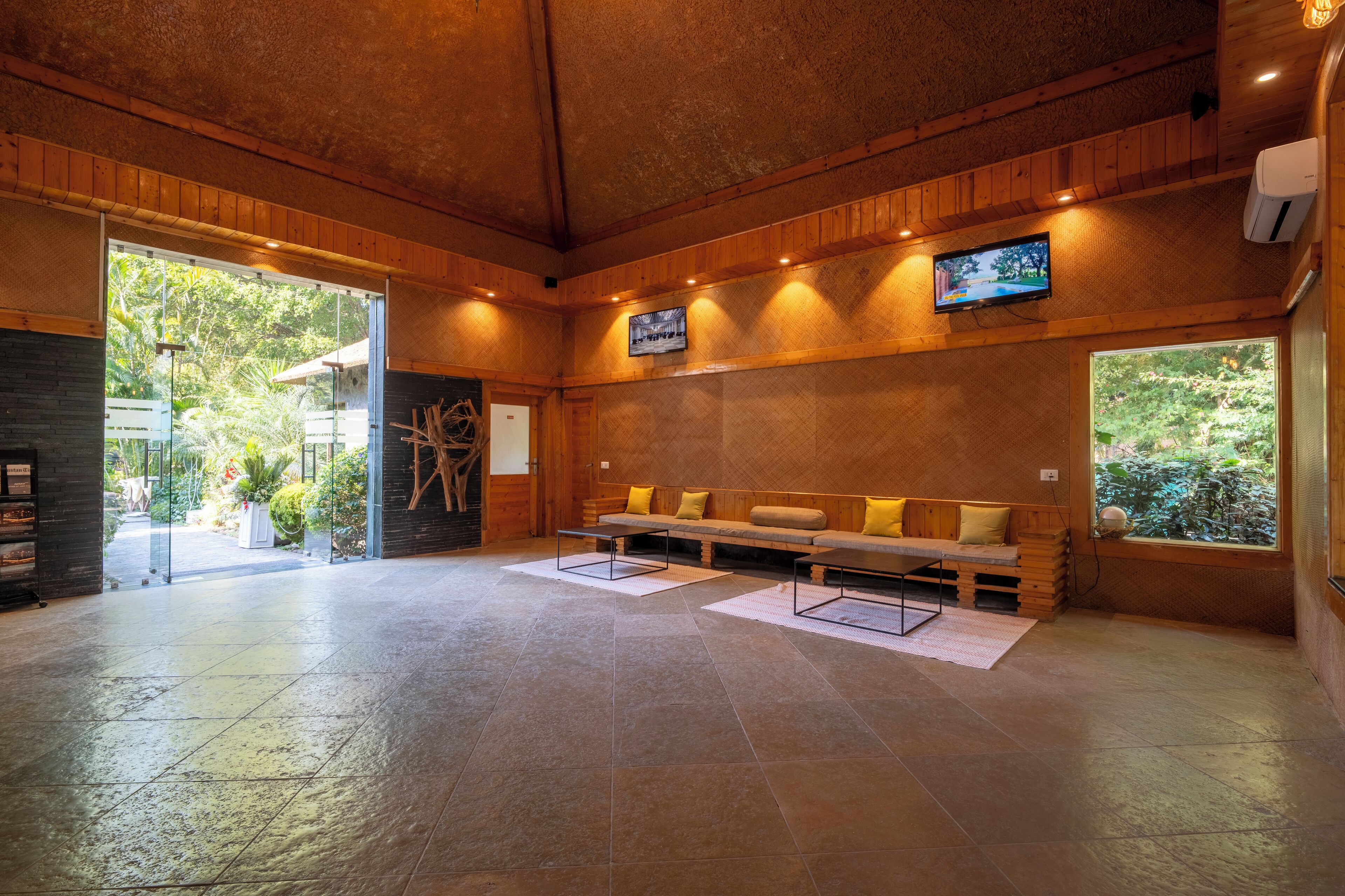 A spacious lobby with a wooden bench seating area, a television mounted on the wall, and a large window providing a view of the outdoors.