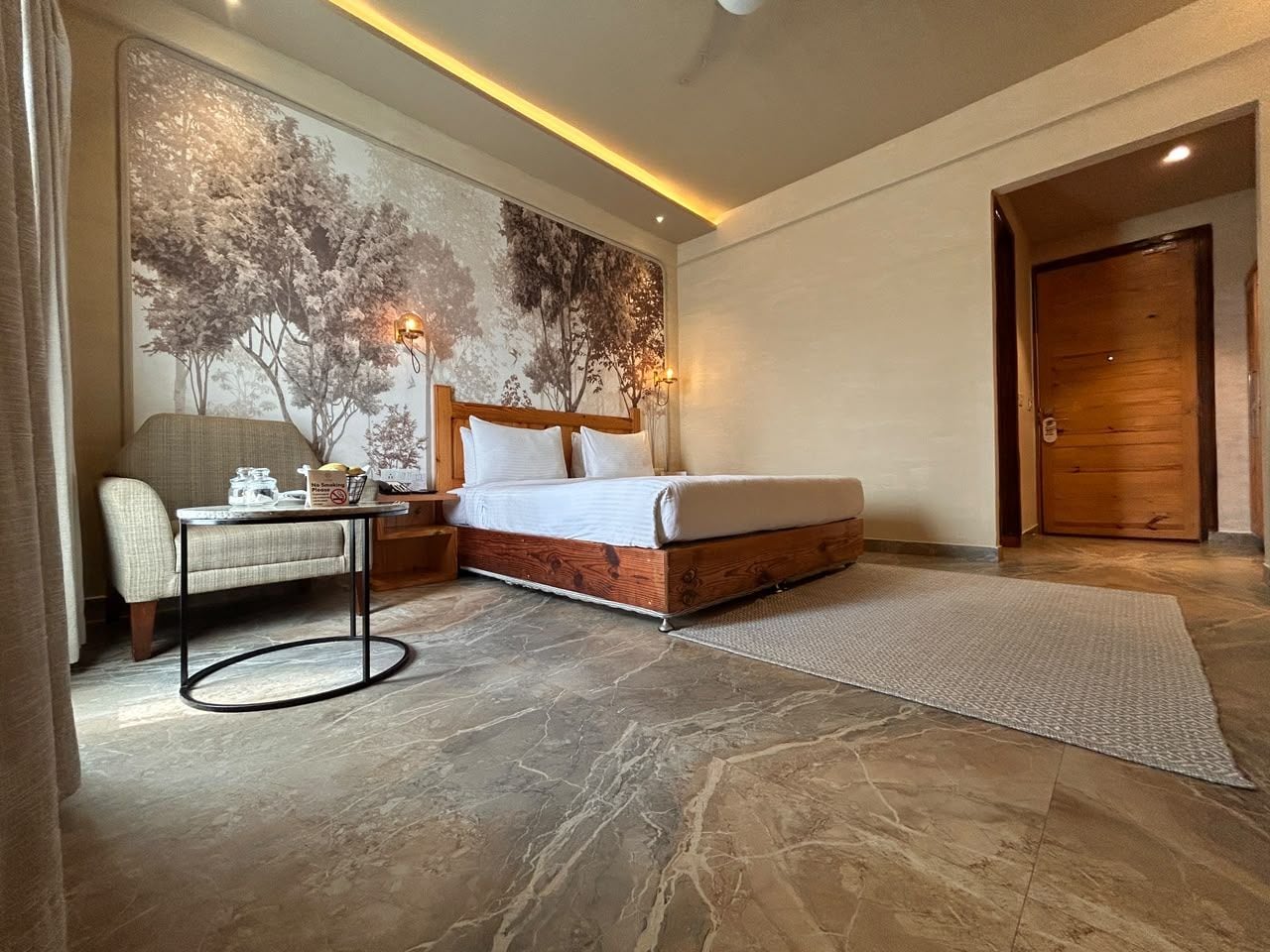A bedroom with a bed, a chair, a table, and a wall mural.
