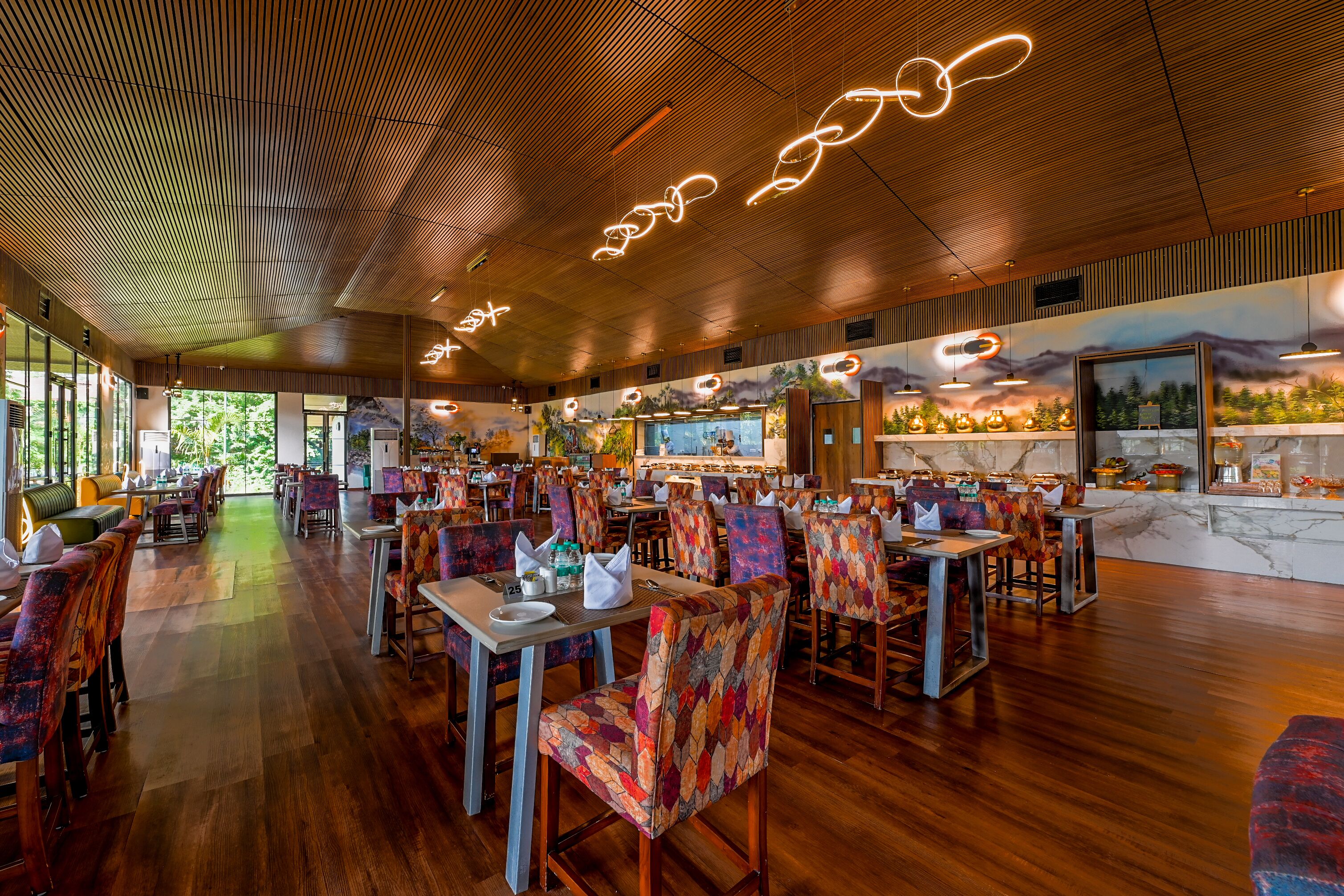 Ein geräumiges Restaurant mit Holzböden, bunten, gemusterten Stühlen und einer Decke mit beleuchteten Linien.