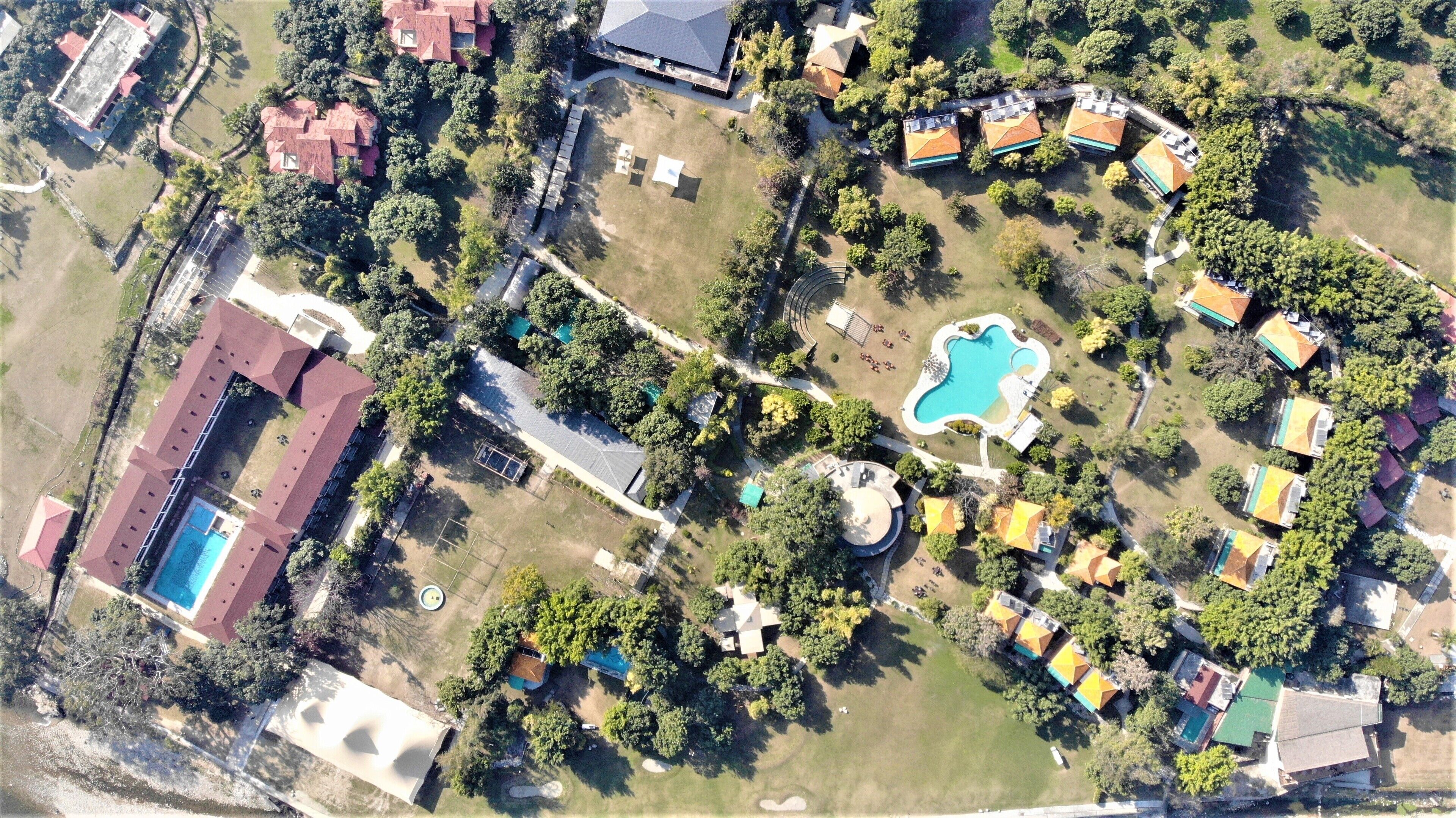An aerial view of a residential area with multiple houses, a swimming pool, and a large building with a red roof.