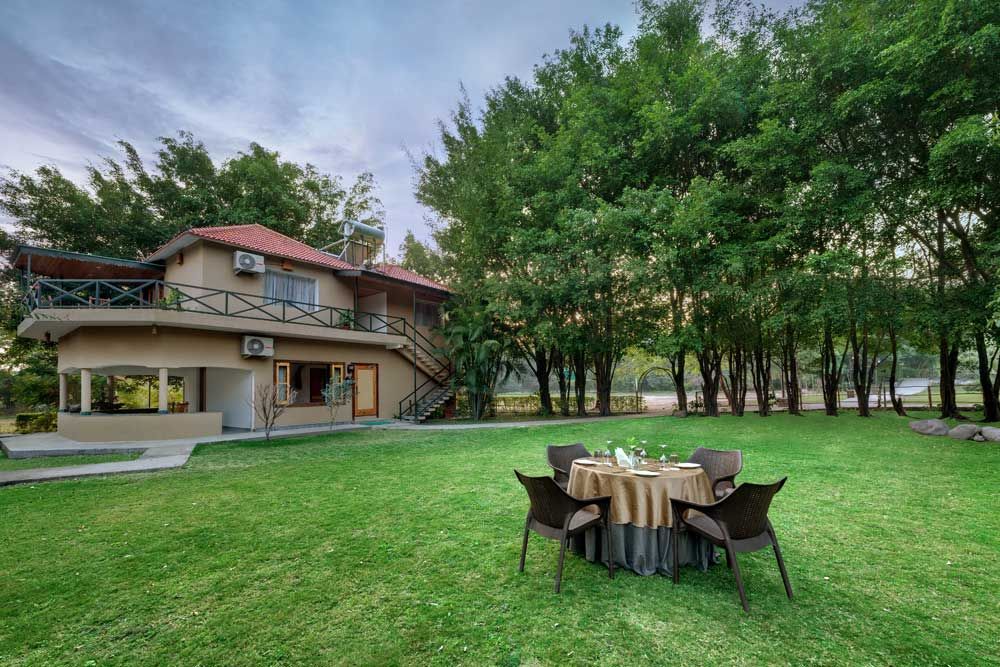 Edificio de dos pisos con un balcón, un área de estar cubierta al aire libre y un jardín con una mesa lista para comer.