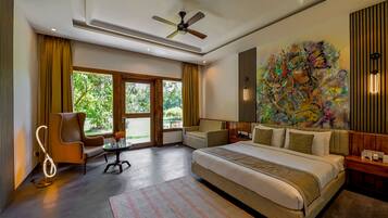 A modern hotel room with a large bed, a ceiling fan, a window with curtains, a painting on the wall, and a small table with a lamp.