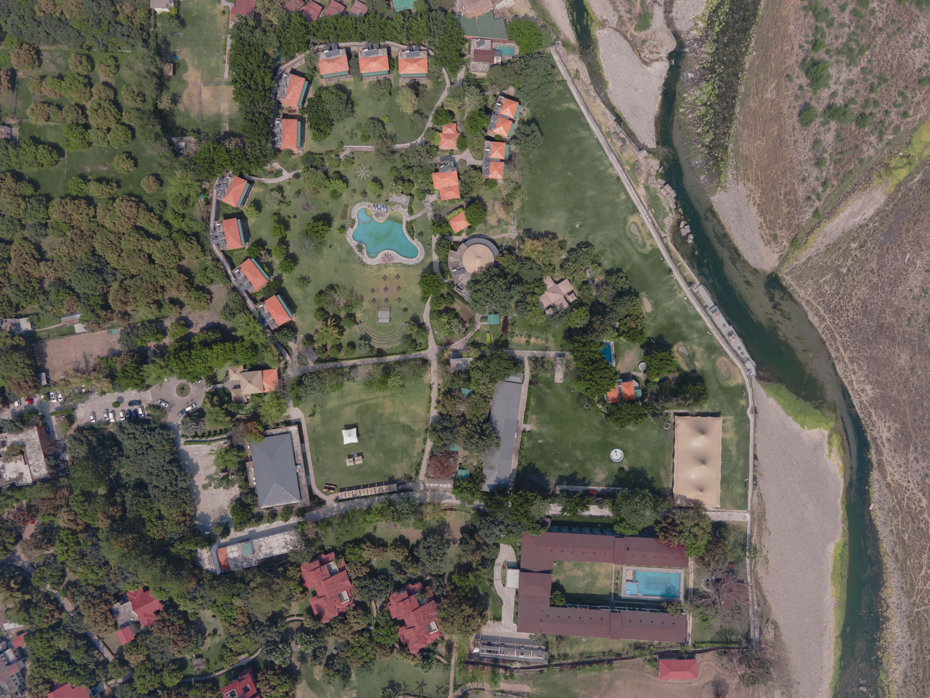 Vista aérea de un complejo turístico con varias edificaciones, una piscina y un río.