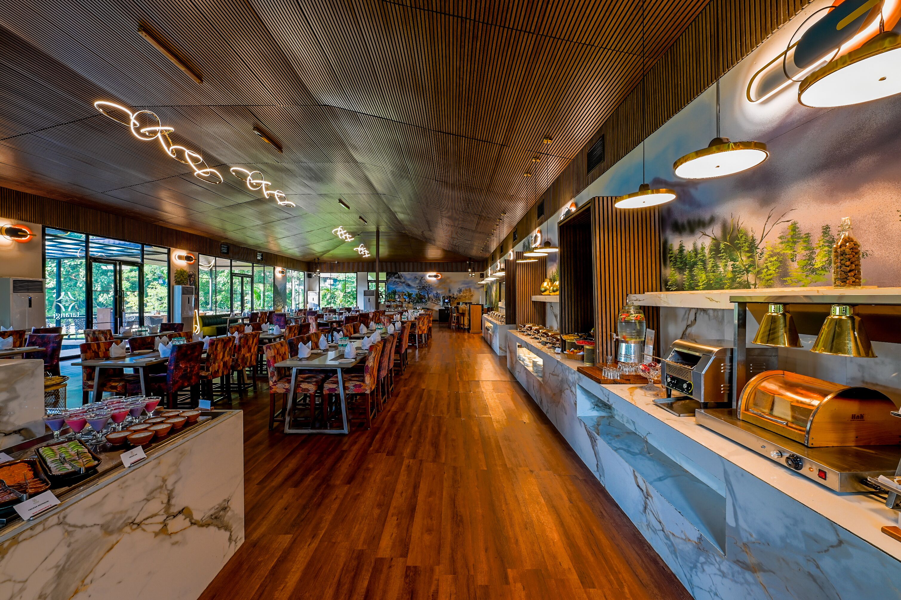 A spacious restaurant with wooden flooring, marble counters, and a long counter with a wood-fired oven.