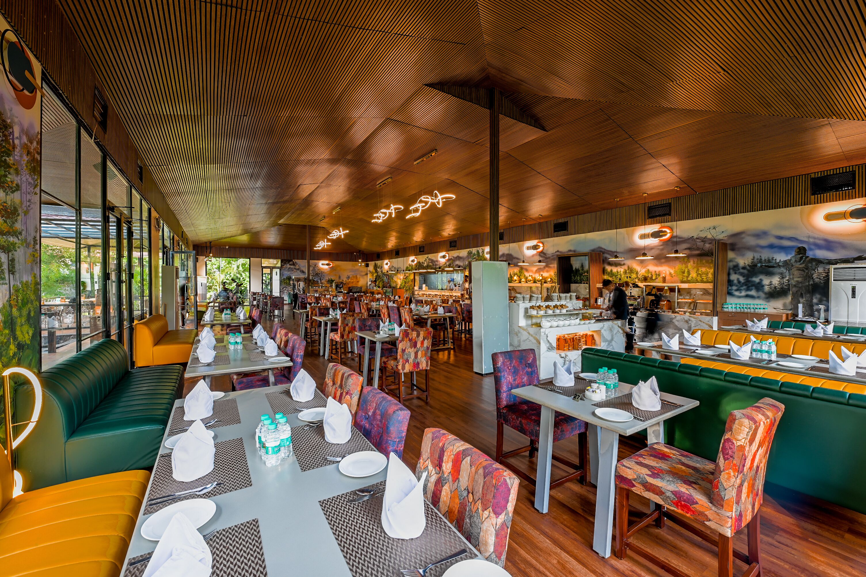 A restaurant with multiple dining areas, including booths and tables, with a modern ceiling design and a mural on the wall.