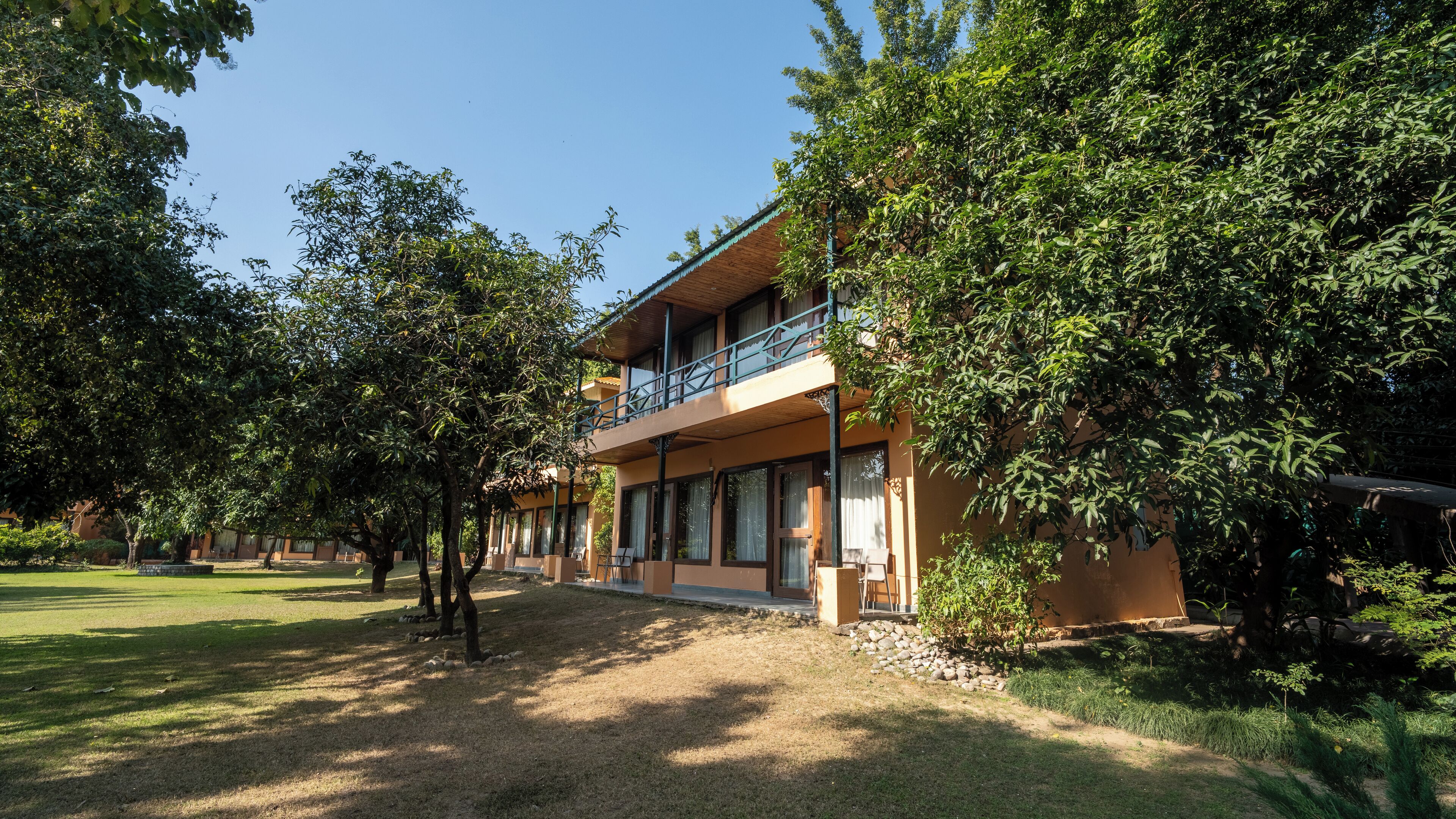 A two-story building with a balcony, surrounded by trees and a well-maintained lawn.