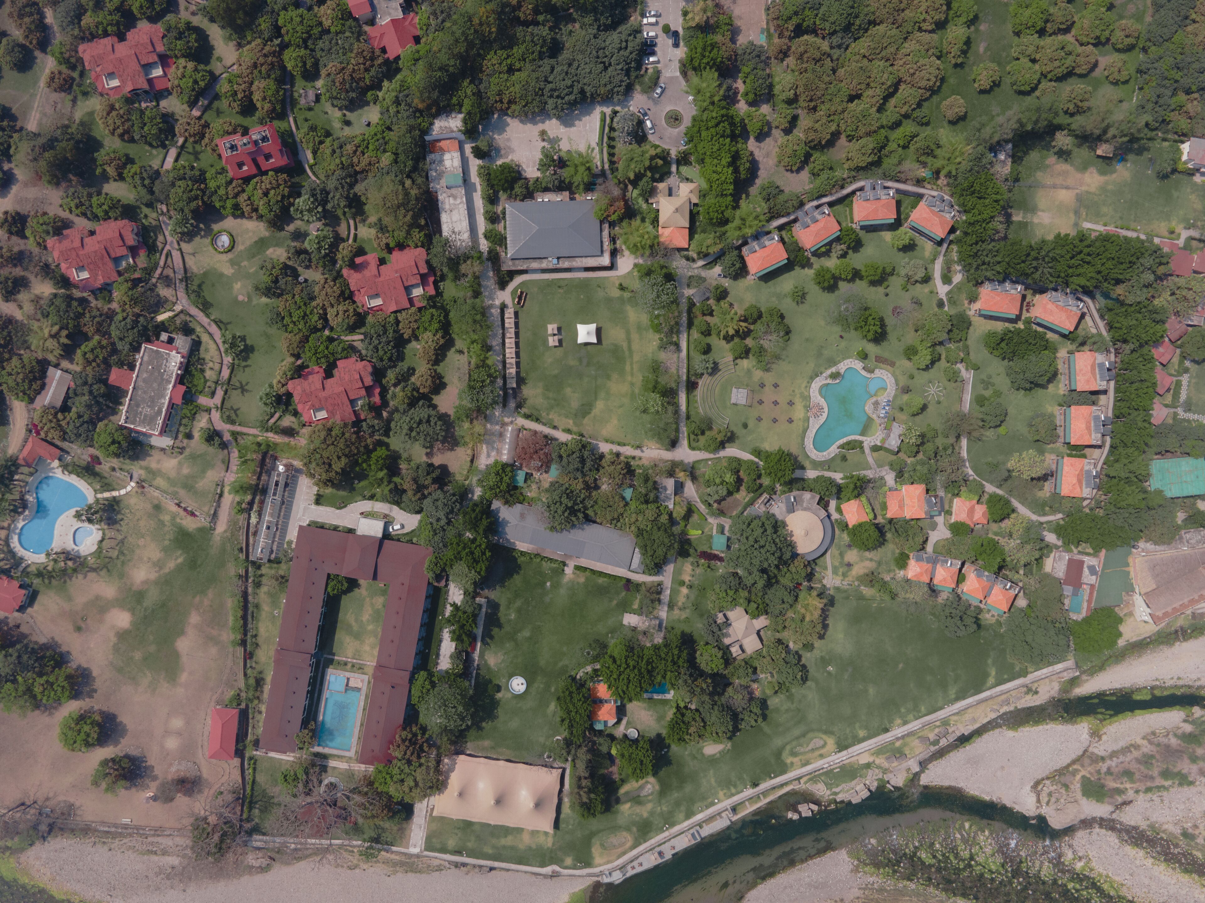 An aerial view of a resort with multiple red-roofed buildings, a swimming pool, and a large open grassy area.