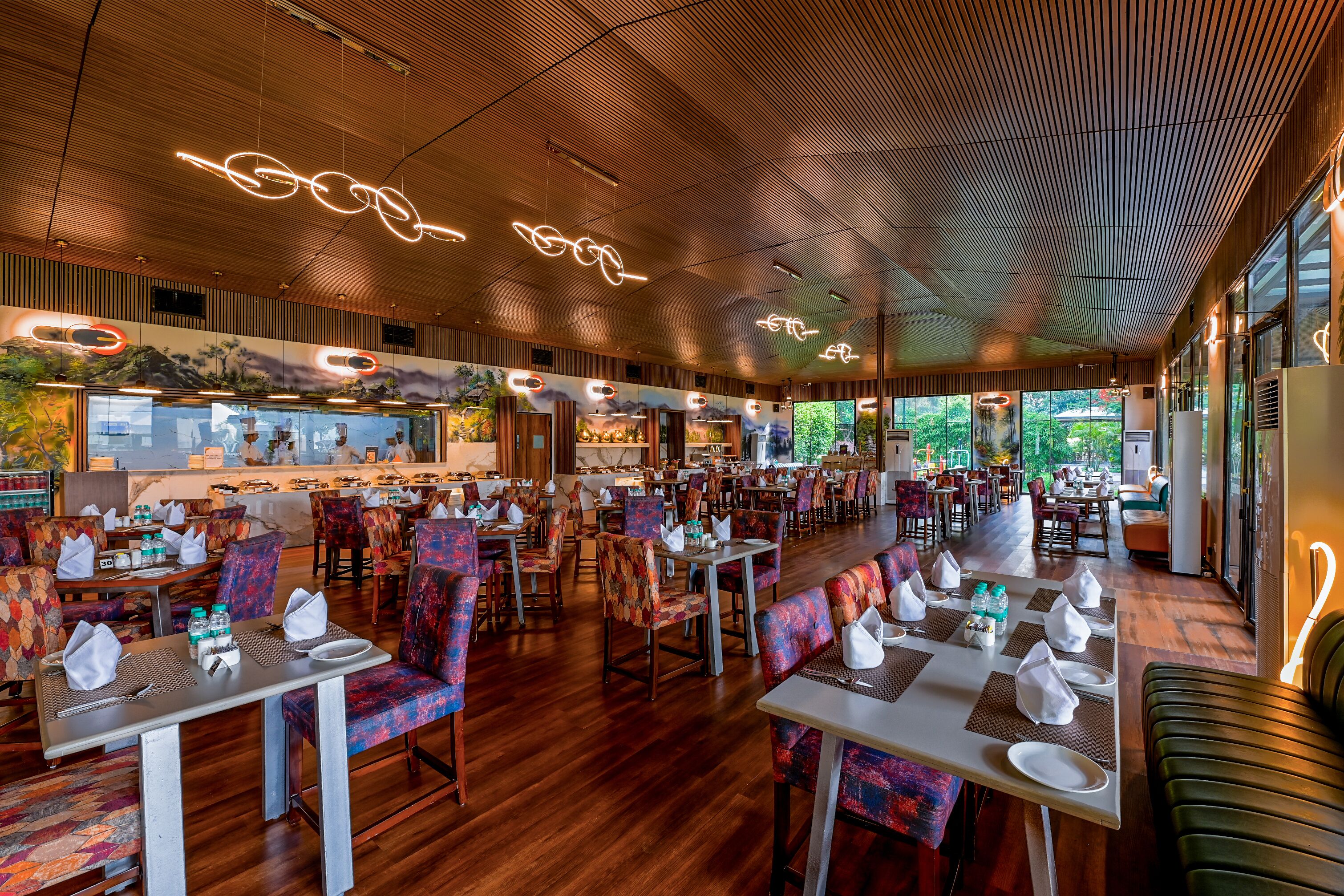 A spacious restaurant with wooden floors, colorful chairs, and a modern ceiling design.