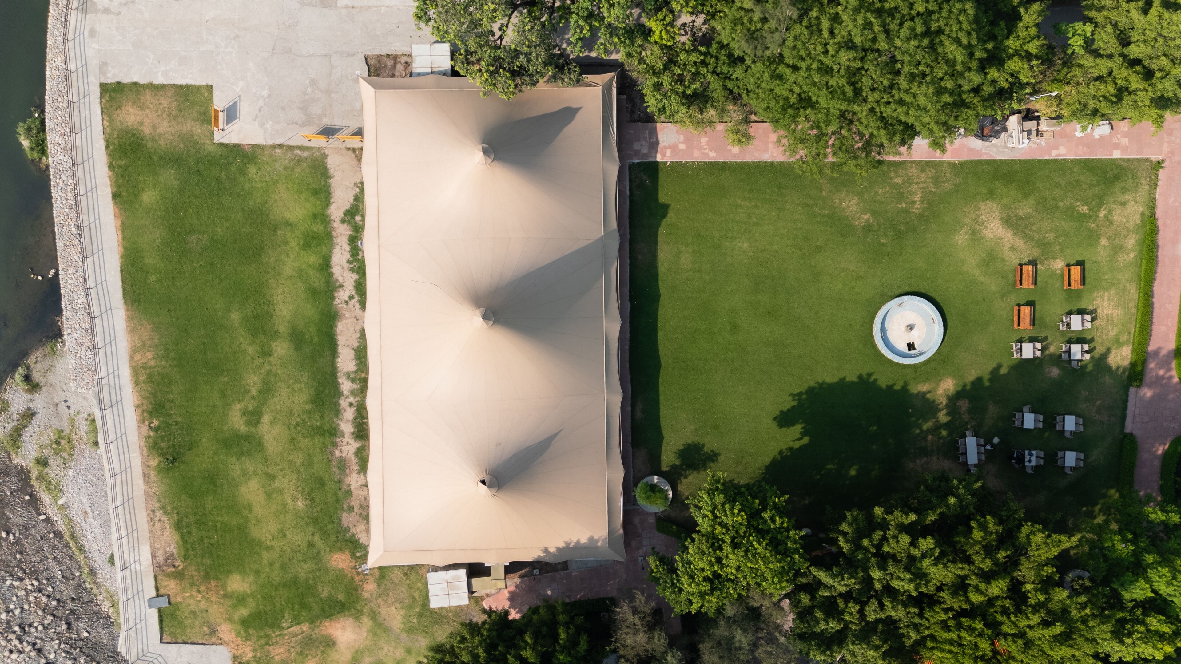 Vista aérea de un parque con una amplia zona abierta, una fuente circular y varias mesas de picnic.