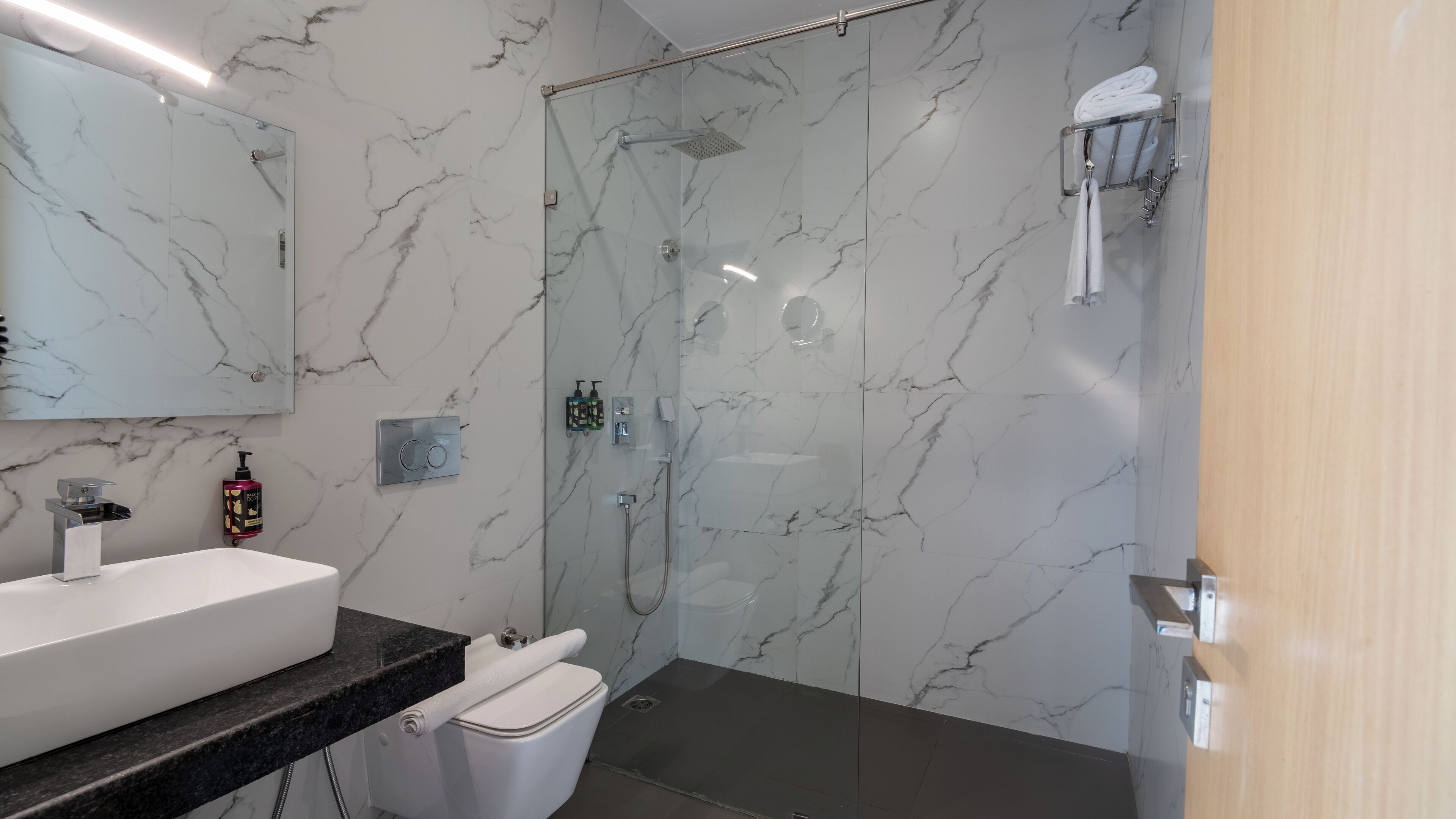 A modern bathroom with a marble backsplash, a glass-enclosed shower, a white sink, and a towel rack.