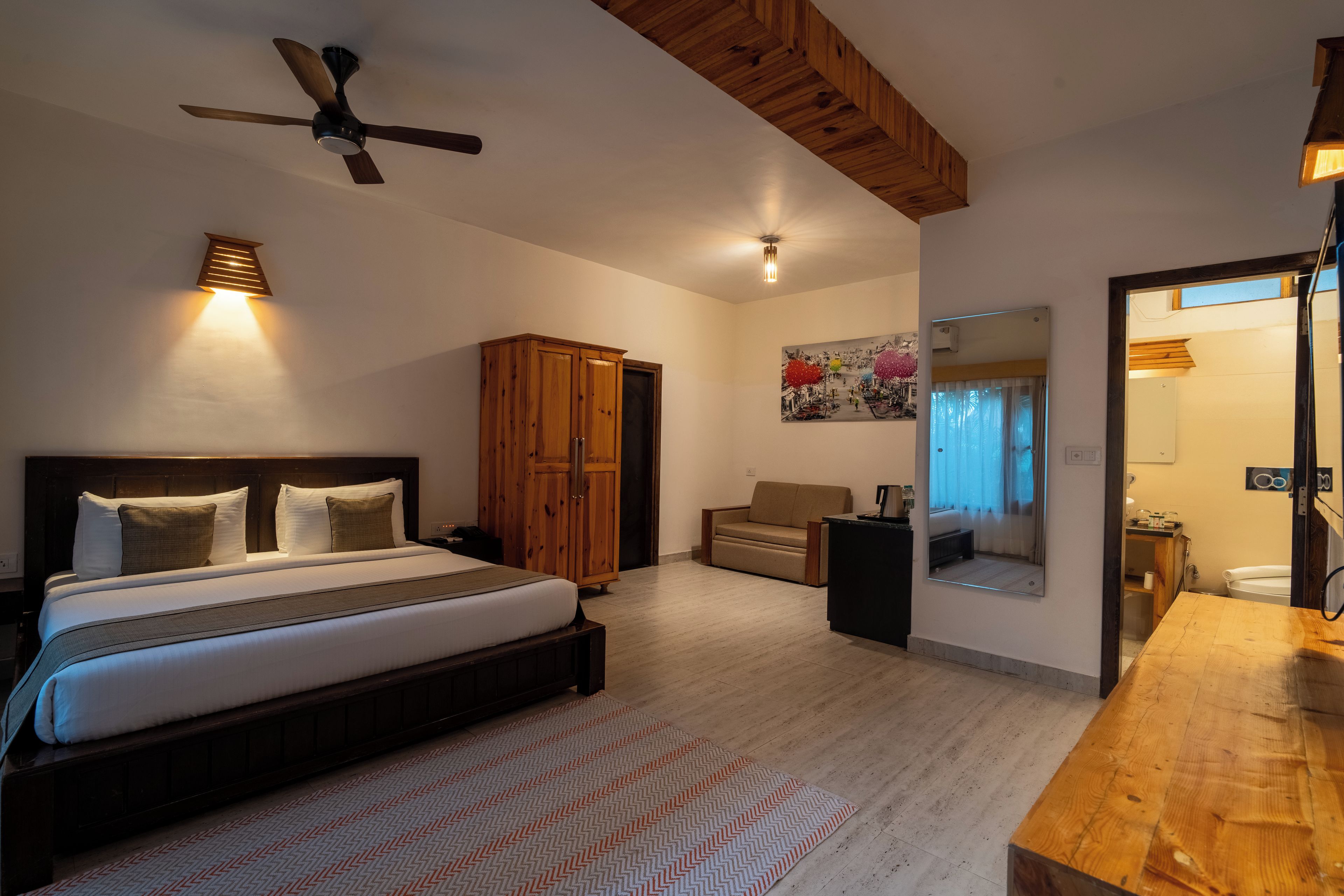 A hotel room with a bed, a wooden wardrobe, a sofa, a small table, and a mirror.