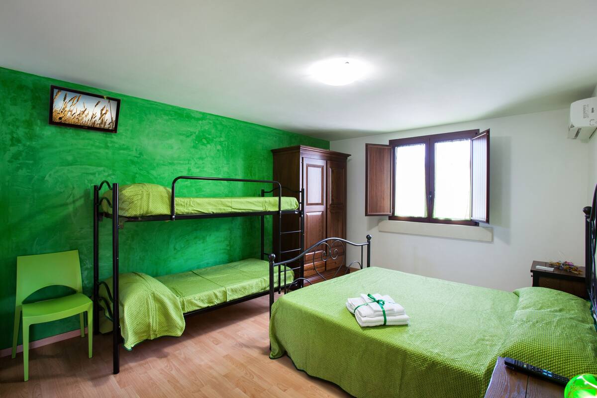 A room with bunk beds, a single bed, a chair, a cabinet, and a window.