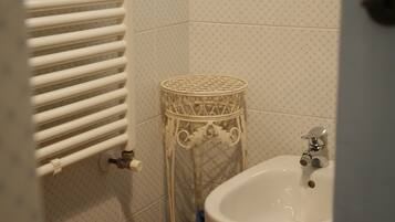 Un baño con un radiador blanco, una cesta de mimbre y un lavamanos.