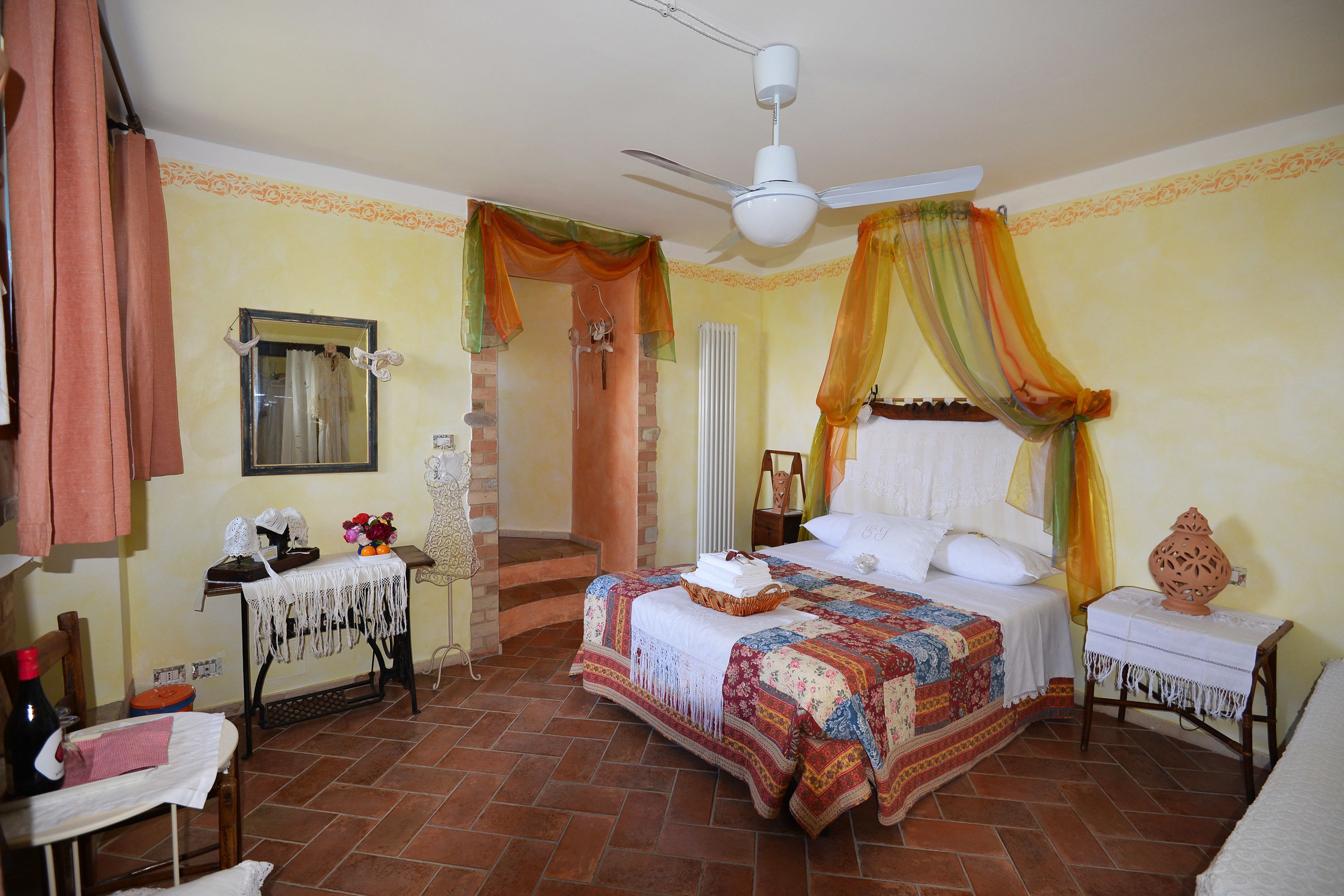 Una camera da letto con un letto, una ventola a soffitto, un comodino, una sedia e un tavolo con una lampada.