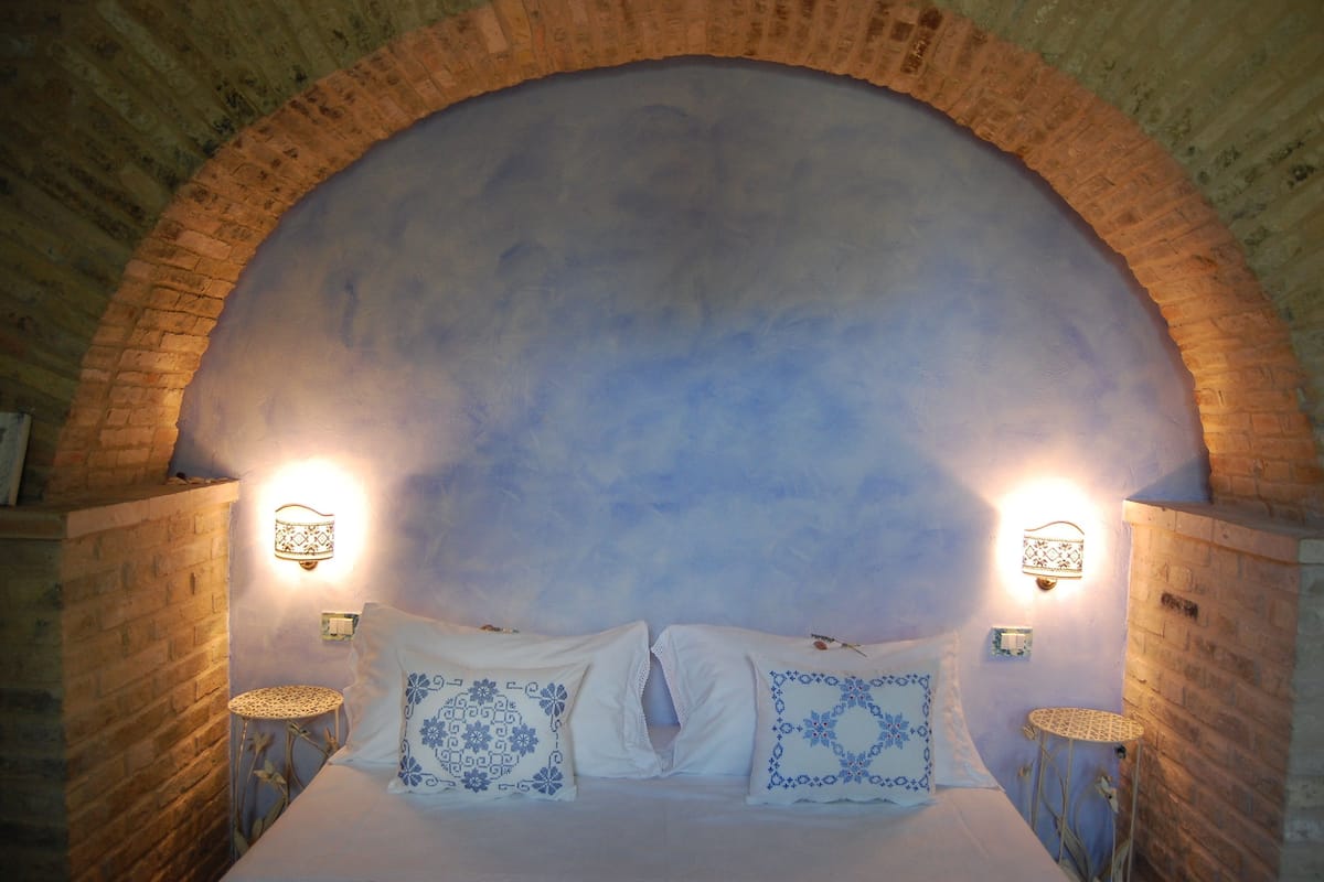 A room with a brick arch ceiling, two bedside lamps, and a bed with patterned pillows.