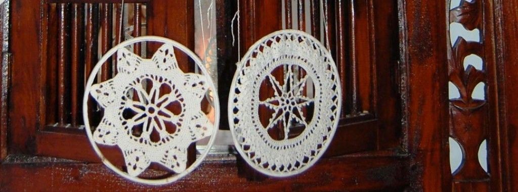 Deux poignées de porte métalliques blanches, de forme circulaire et dotées de motifs complexes, sont fixées à une porte en bois ornée de panneaux verticaux.