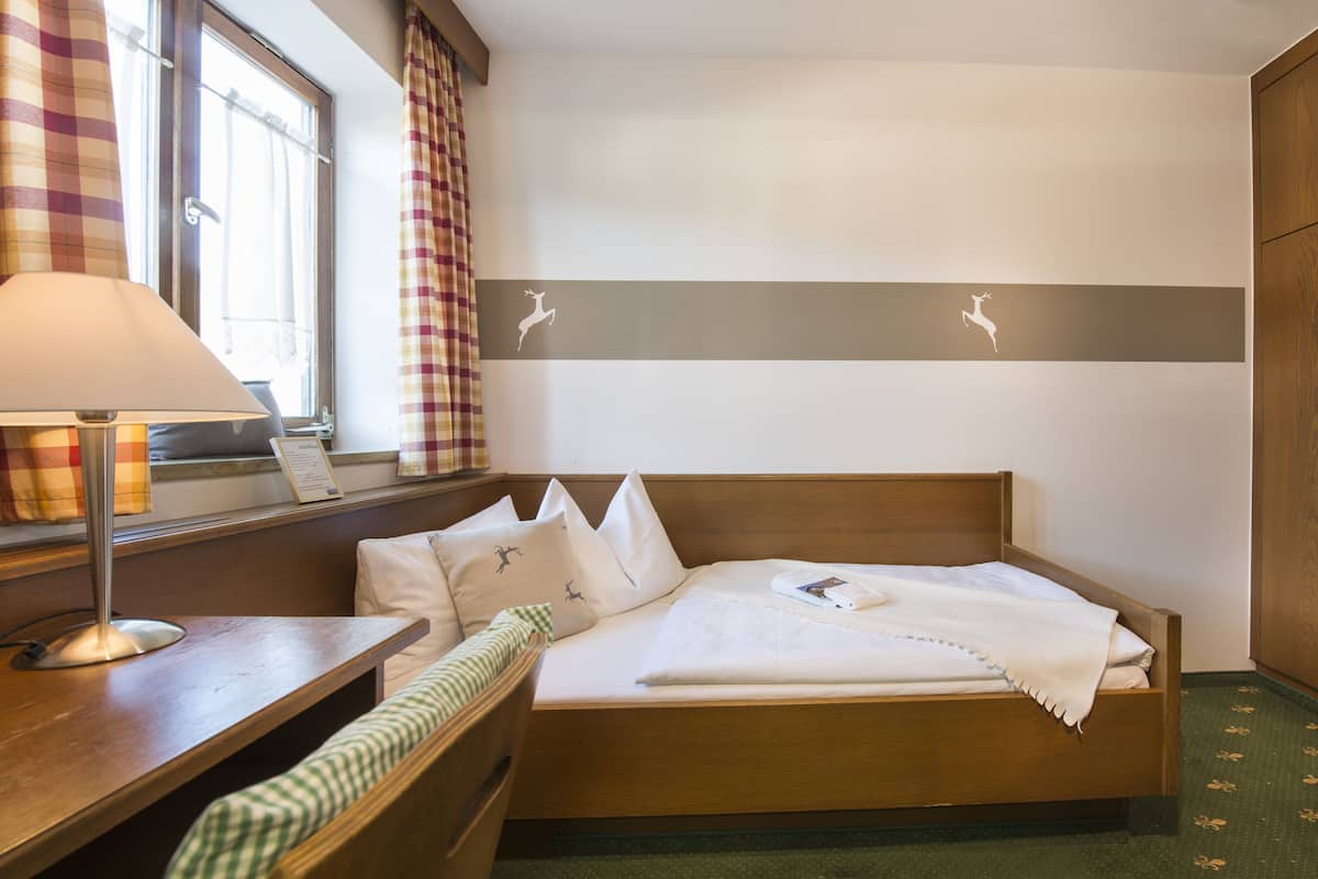 A neatly made bed with a white comforter and pillows, a bedside table with a lamp, and a window with curtains.
