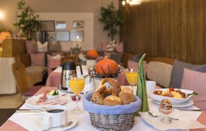 A breakfast setting with a basket of bread, a pumpkin, and orange juice on a table. - Hotel Jägerhof Garni (Bernau am Chiemsee)