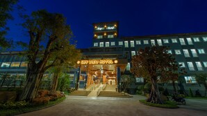 Entrada de hotel con una escalera que conduce al vestíbulo, rodeada de árboles y un jardín cuidado.
