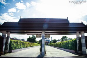 A covered entrance to Skyview Resort in Buriram with a traditional roof structure, directional signs, and a pathway flanked by hedges. - Sky View Resort Buriram (Buriram)