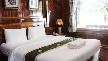 A neatly made bed with white linens, a green decorative runner, and a folded towel on the foot of the bed. There is a wooden headboard, a framed picture on the wall, and a lamp on a bedside table.