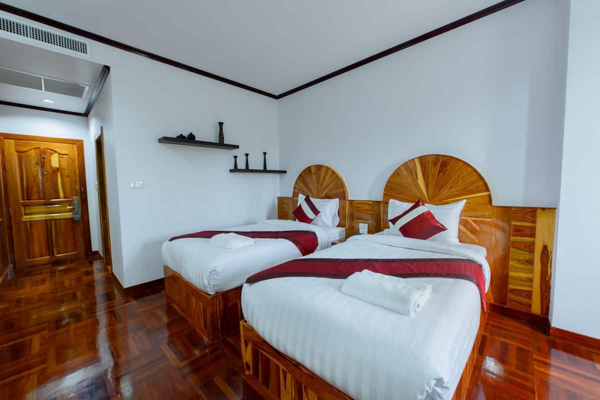 A hotel room with two wooden beds, white bedding, a wooden door, and a shelf with decorative items.