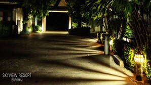 Vista nocturna de la entrada del Skyview Resort, con un sendero que conduce a un edificio, rodeado de vegetación e iluminado por farolas.